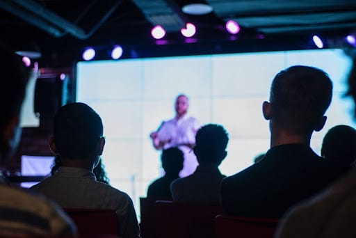 Speaker wearing white standing in front of people on stage