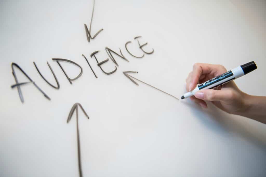 a hand writing the word audience on a whiteboard