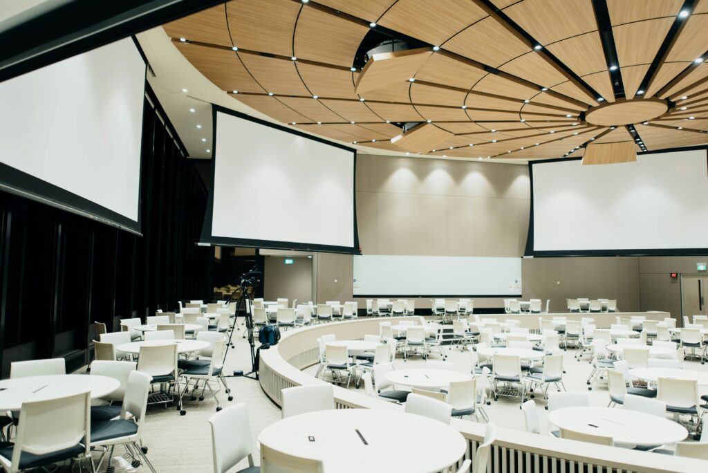 The scene shows a conference room with event technology tools, including projectors, screens, and sound systems set up for corporate event planning